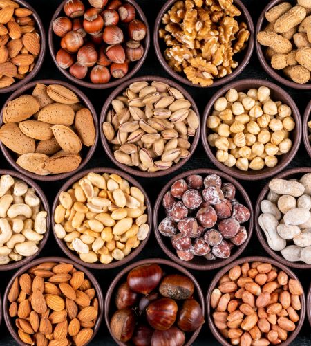 Set of pecan, pistachios, almond, peanut, cashew, pine nuts and lined up assorted nuts and dried fruits in a mini different bowls on a black stone background. flat lay.